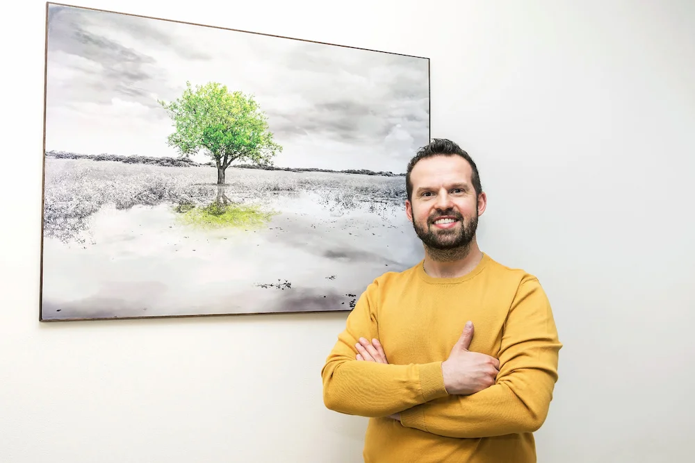 Jan Melichárek poradce v investičním poradenství u obrazu s velkým stromem, který symbolizuje dlouhodobé investice.